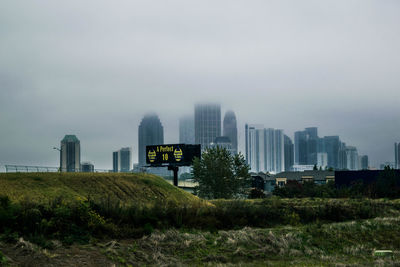 View of field and buildings against sky