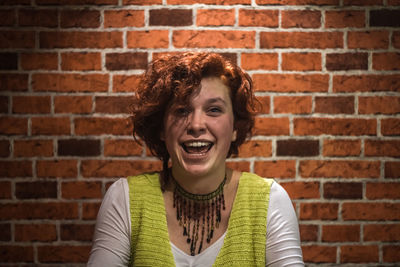 Portrait of happy young woman against brick wall