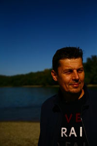 Portrait of smiling man against lake against clear blue sky