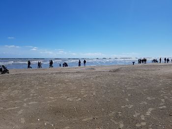 People on beach against clear blue sky