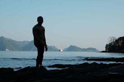 Man on rock by sea against clear sky