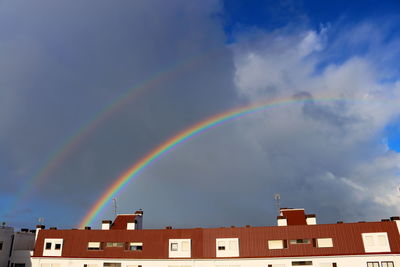 A radiant double rainbow forms over a high-rise apartment building under dark thunderclouds 