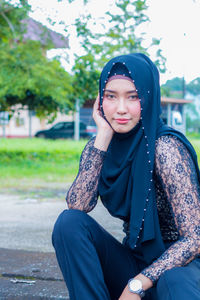 Portrait of young woman with hand on chin sitting outdoors