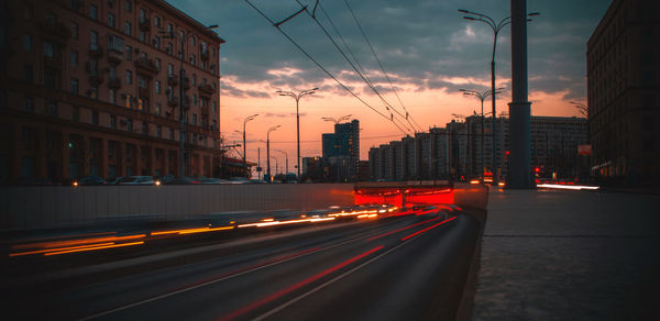 Light trails on road in city against sky during sunset