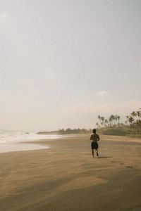 Rear view of man walking on field against clear sky