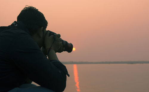 Silhouette man photographing sea against sky during sunset