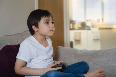 Boy playing game while sitting on sofa at home
