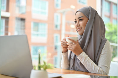 Businesswoman wearing hijab holding coffee cup at cafe