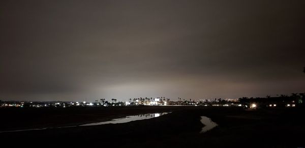 Illuminated buildings by sea against sky at night