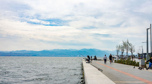 People on road by sea against sky