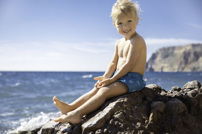 Portrait of young woman sitting on rock at beach