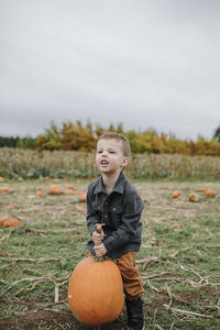 Cute boy lifting heavy pumpkin while standing on field