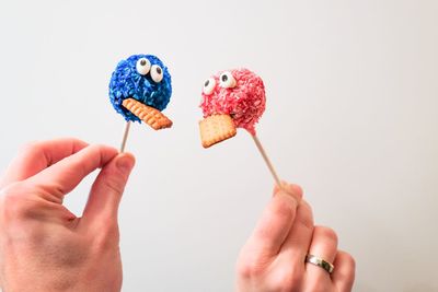 Cropped hands of man and woman holding cake pops against wall