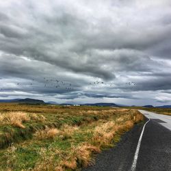 Road passing through field against cloudy sky