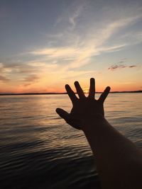 Close-up of silhouette hand against sea during sunset