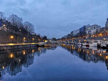 Illuminated bridge over river in city against sky during winter