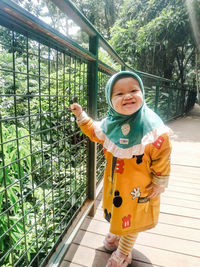 Cute boy standing by railing against trees