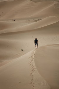 Rear view of man walking on sand dune