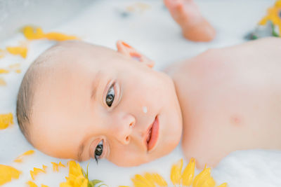 Portrait of cute baby lying on milk bath with flowers 