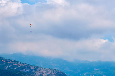 Low angle view of people paragliding against sky