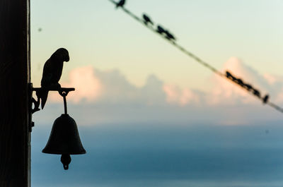 Silhouette bird perching on pole against sky during sunset