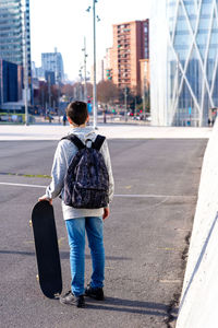 Rear view of a boy with backpack and skateboard standing on street