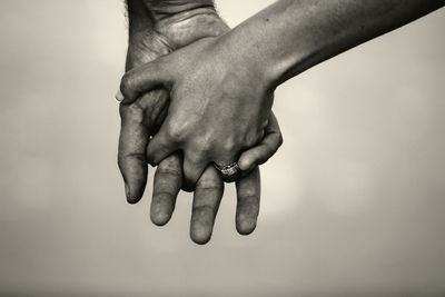 Close-up of cropped holding hands against white background