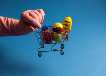 Cropped hand of woman holding miniature shopping cart against blue background