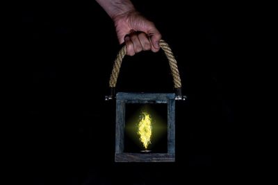 Cropped hand holding illuminated lantern against black background