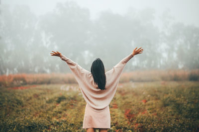 Rear view of woman standing against trees during foggy weather