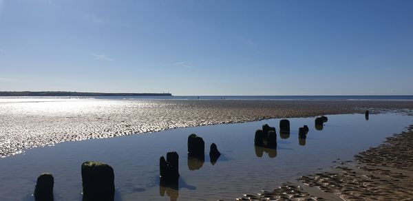 Wooden posts in sea against sky