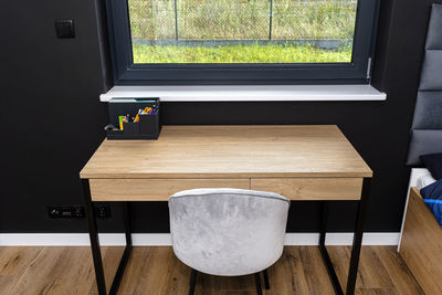 A wooden table with chair under the window in a modern boy room in black and white colors. 