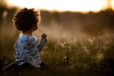 Girl sitting on field during sunset