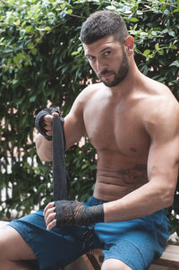 Close-up of shirtless boxer sitting against plants