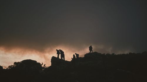 Silhouette people standing on rock against sky