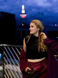 Young woman standing at building terrace in city during dusk