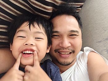 Portrait of father and son smiling while lying on bed