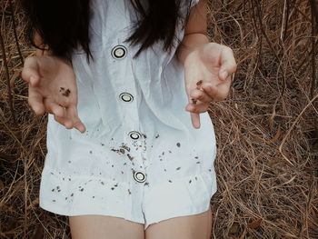 Midsection of woman sitting on dried plants in forest