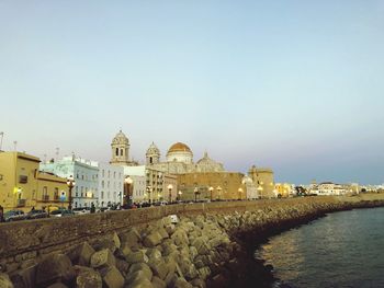 Buildings by sea against clear sky