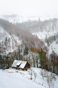 Scenic view of cabin and snowcapped mountains in a winter foggy day