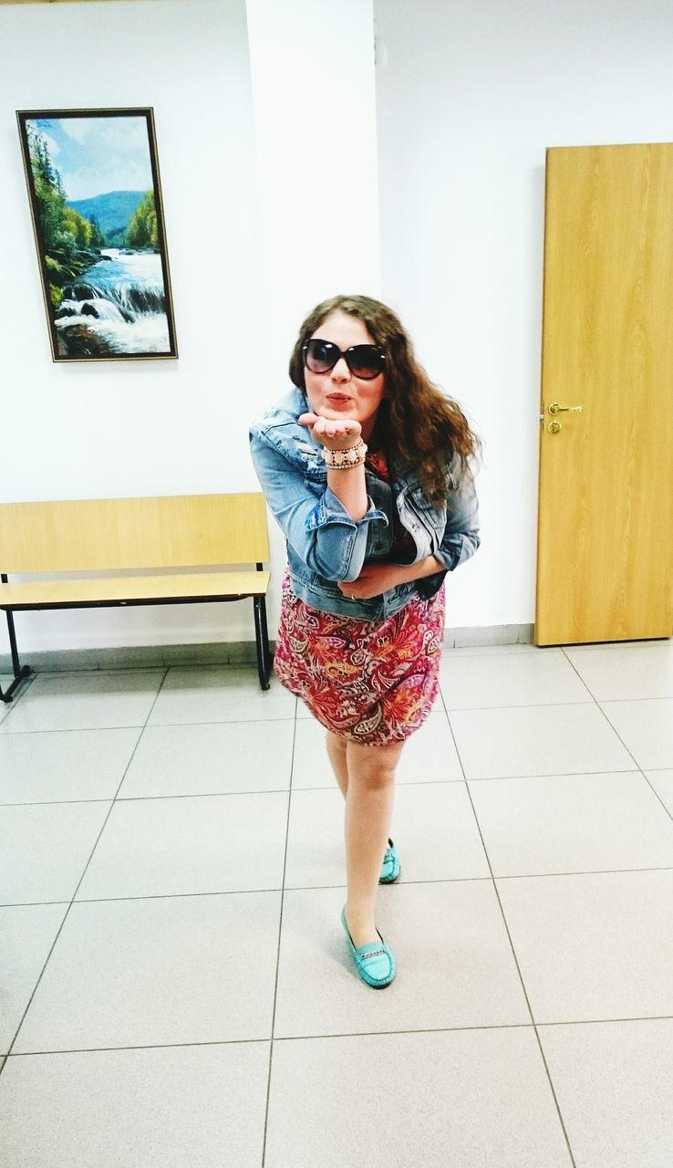 PORTRAIT OF A YOUNG WOMAN STANDING ON TILED FLOOR