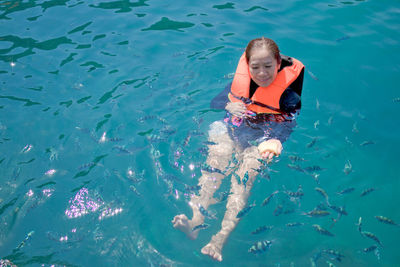 Woman wearing life jacket in a tropical sea and feeding fish