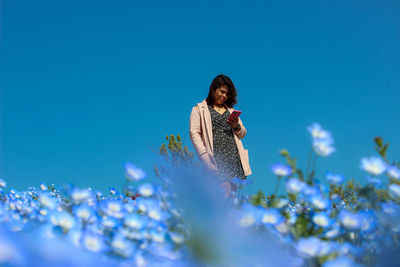 Young woman on flowering plants against blue sky