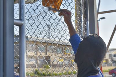 Rear view of boy looking through chainlink fence