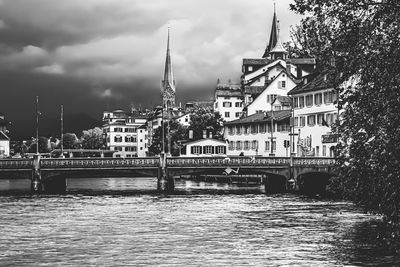 Bridge over river by buildings against sky