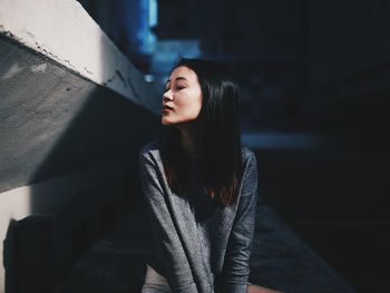 Close-up of woman sitting by retaining wall with eyes closed