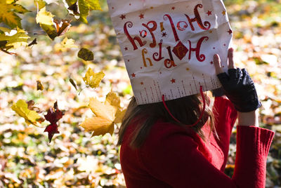 Side view of woman covering face with paper bag in autumn during sunny day