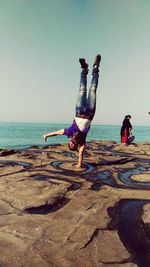 Man doing handstand at beach against sky
