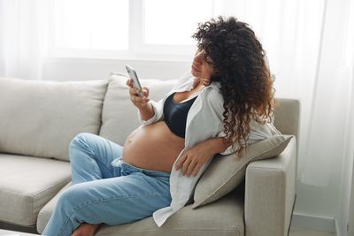 Young woman using mobile phone while lying on sofa at home