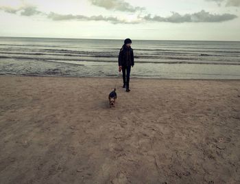 Woman with dog on beach against sky